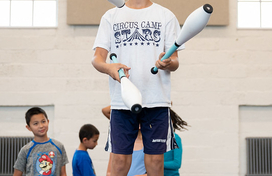 Boy juggles bowling pins while balancing on a ball