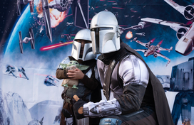 An adult dress in a Mandalorian costume posing for a photo with a child in same costume. 