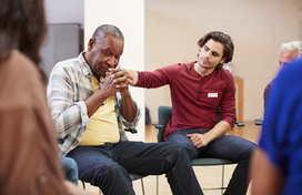 Younger man consoling older man in a support group.