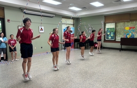6 kids dressed in maroon shirts and black shorts doing a jump rope routine