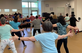 Group of older adults in an exercise class. They are facing away with their arms raised up to their sides.