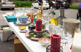 Table at yard sale with a variety of items including candles and mugs.