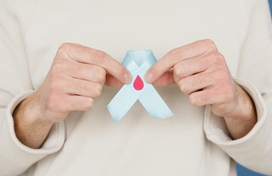 Caucasian person holding up light blue ribbon with blood droplet in their hands. No face shown.