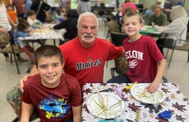 Older adult white male with two kids elementary school age, all wearing red t-shirts posing together smiling at an arts & crafts table.