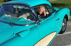 Older white woman sitting in the driver seal of a teal and cream colored classic car.