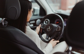 Inside view of woman driving car with hands on steering wheel.