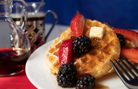 Waffles on a plate with strawberries and blackberries and syrup and butter.