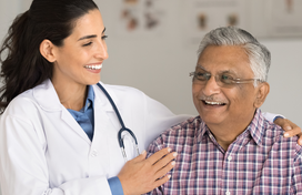 An older man with light brown skin is seen by a smiling doctor with long brown hair. 