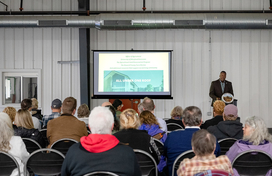 Howard County Executive Calvin Ball standing at a podium inside a Howard County Fairgrounds building delivering his State of Agriculture address to the county's farming community.