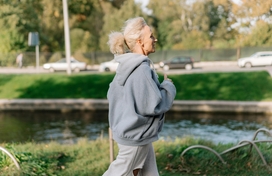 Caucasian women with light colored hair in pony tail running in a grey sweatshirt outside.