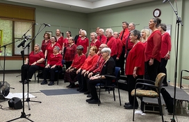 Group of about 25 older adult men and women all wearing red performing songs