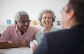 Black older adult male with Caucasian older adult female meeting with man at table.