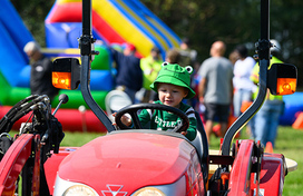 Child in a frog costume sitting on and playing with a red tractor