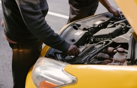 an open hood on a yellow car with two hands touching car parts inside the hood