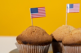 American flags on toothpicks sticking out of muffins surrounded by blueberries on a blue plate
