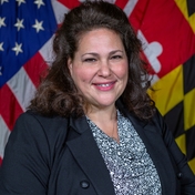Headshot of woman with long dark hair wearing black blazer - Ofelia Ross Ott