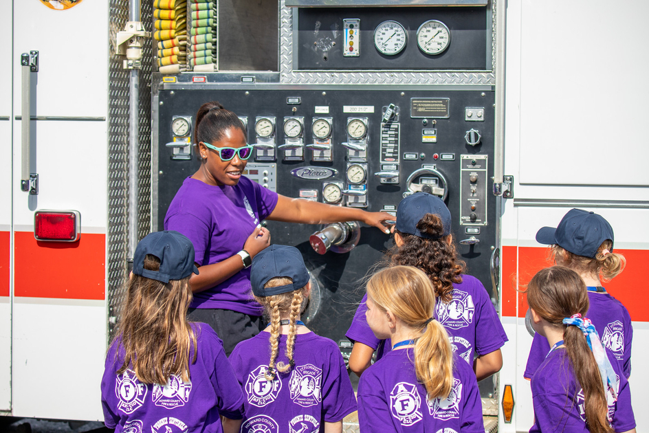 Firefighter explains pump panel on fire engine to campers.