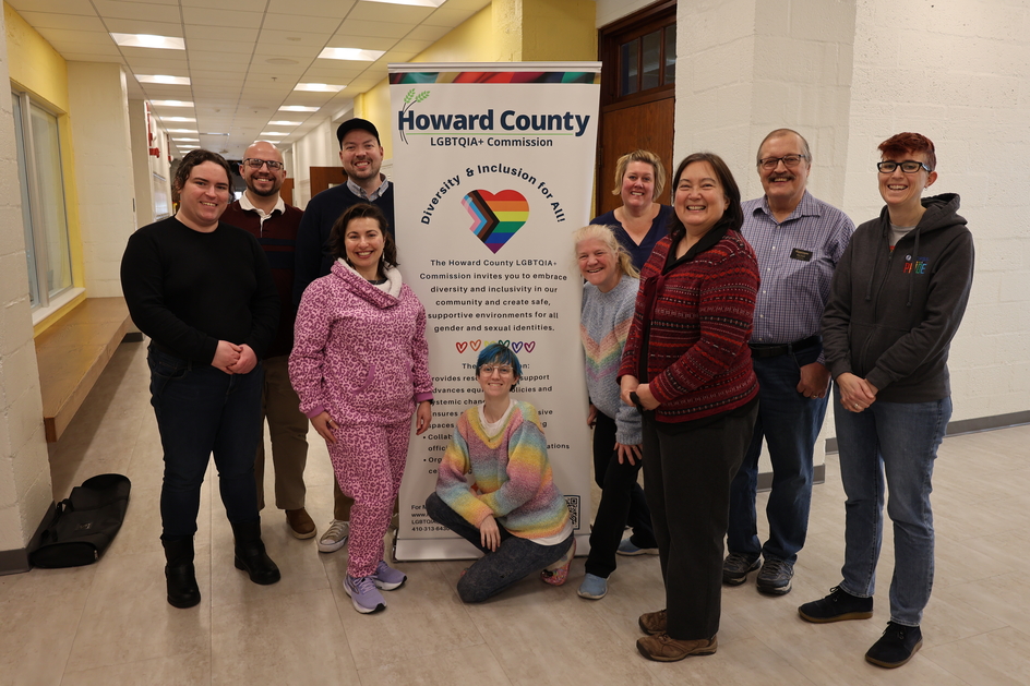 10 people stand posed with a banner reading "Howard County LGBTQIA+ Commission". 