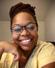 Photo of Jessica Chaney smiling with glasses, yellow shirt, and hoop earrings.