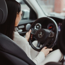 Inside view of woman driving car with hands on steering wheel.