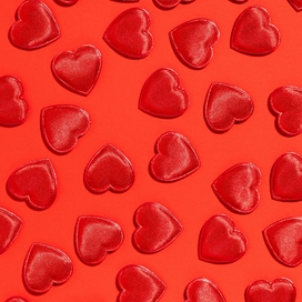 Shiny red cut out hearts on a lighter red background.