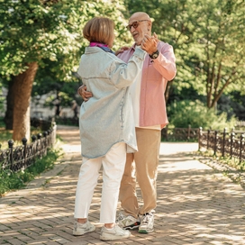 Older adult couple dancing on a sidewalk in a park on a nice day.