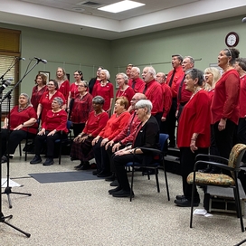 Group of about 25 older adult men and women all wearing red performing songs