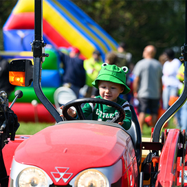 Child in a frog costume sitting on and playing with a red tractor