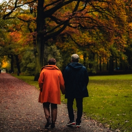 man and woman walking surrounded by leaves on the ground and trees changing to autumnal colors