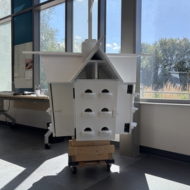 white 3-story birdhouse sitting by a window in a workspace