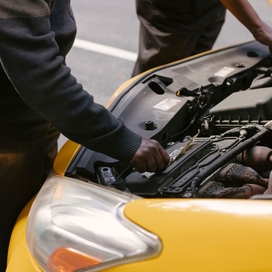 an open hood on a yellow car with two hands touching car parts inside the hood