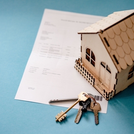 teal background with a sheet of paper, keys, and a small model home with the latter two items being on top of the paper