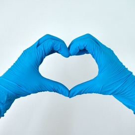 two blue-gloved hands form a heart shape in front of a white background