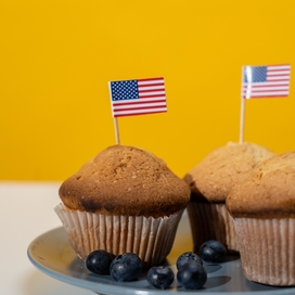 American flags on toothpicks sticking out of muffins surrounded by blueberries on a blue plate